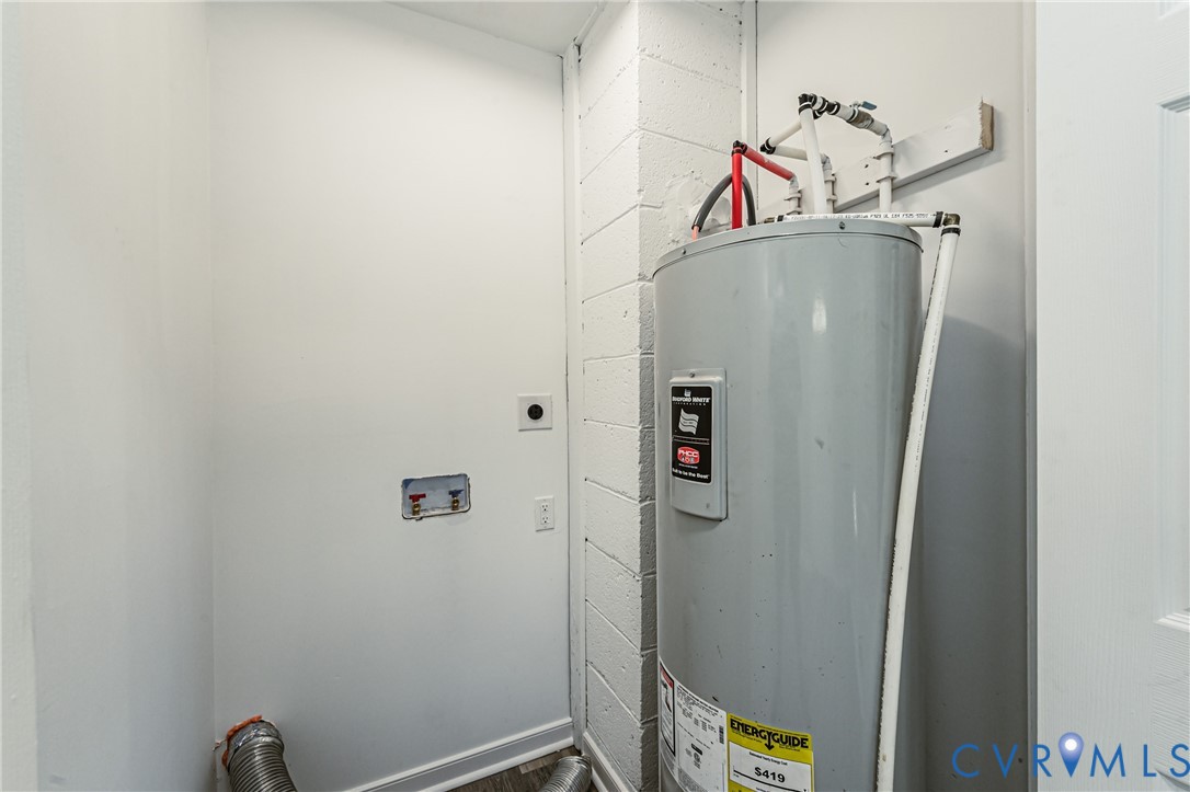 Utility area featuring a cylindrical water heater, exposed concrete block wall, and dedicated plumbing connections