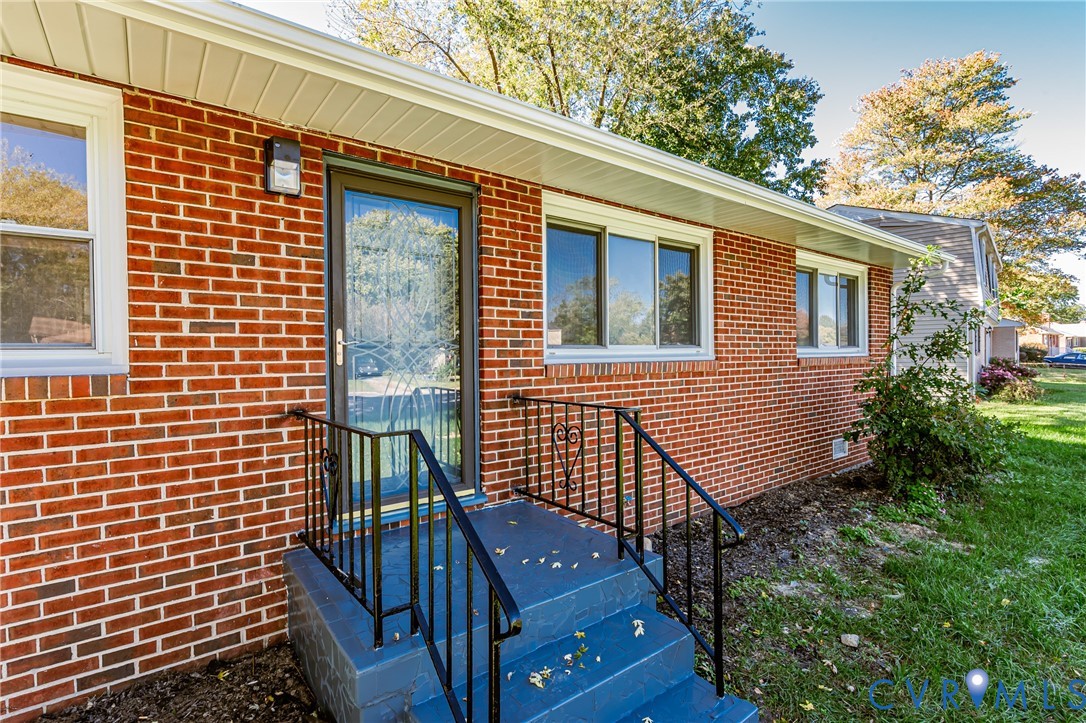Red brick exterior featuring painted concrete stairs, black metal railings, a storm door with glass detailing, and vinyl window frames