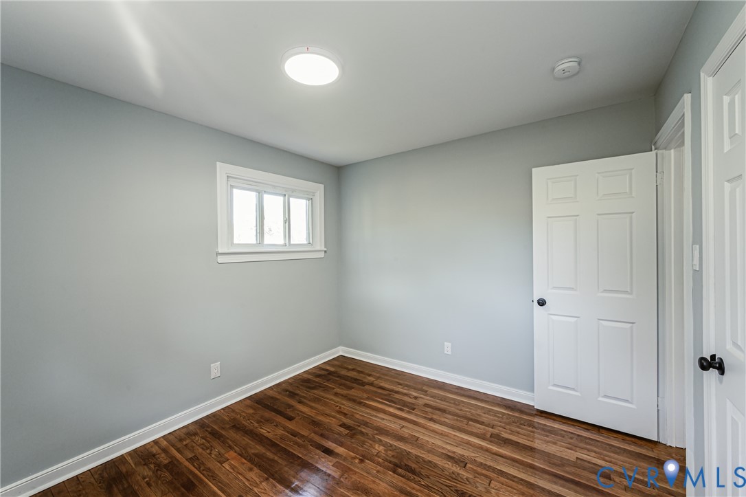 Room featuring wood-finish flooring, neutral wall paint, a six-panel door with matte black hardware, and a single-hung window with white casing