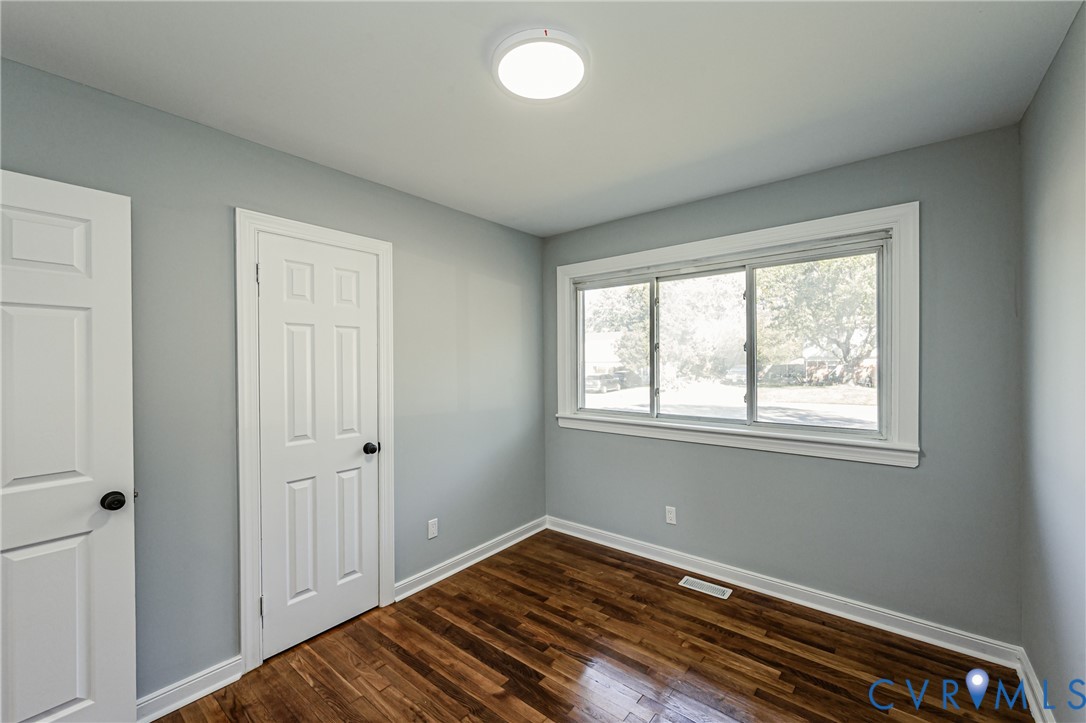 Room featuring wood-finish flooring, neutral wall paint, two white six-panel doors, a large sliding window, and a central flush-mount ceiling light