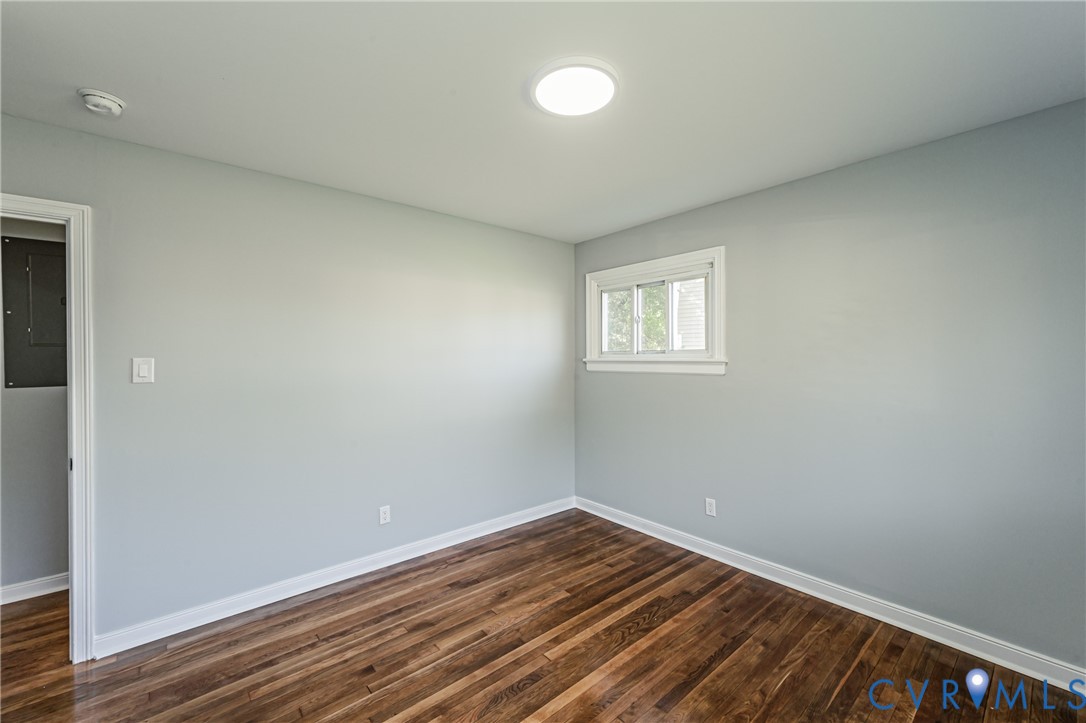 Room interior featuring wood-finish flooring, neutral wall paint, and a white-trimmed sliding window