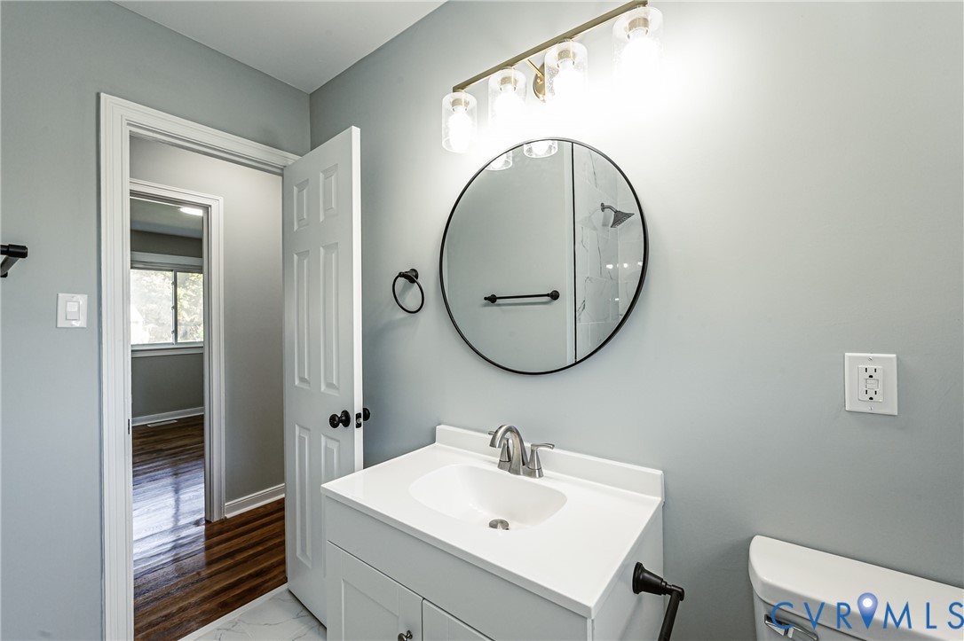Bathroom vanity featuring a white cabinet, integrated sink, and polished metal faucet, accented by a circular black-framed mirror, four-light glass fixture, and matte black hardware
