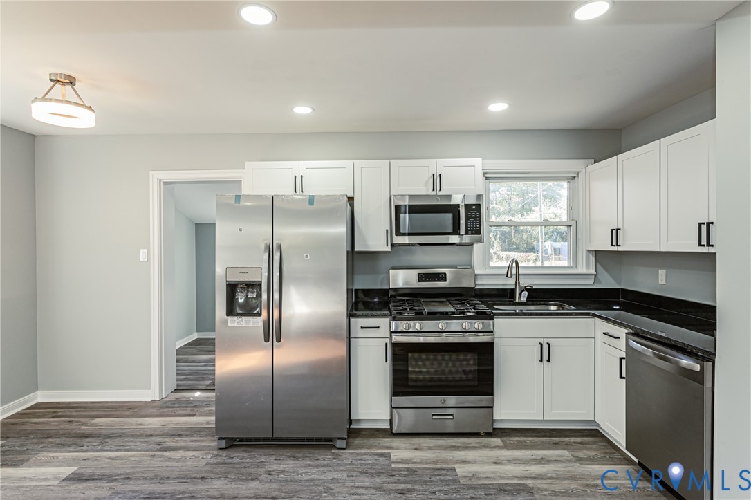 Kitchen featuring white shaker-style cabinetry, dark stone countertops, stainless steel appliances, recessed lighting, and wood-finish flooring