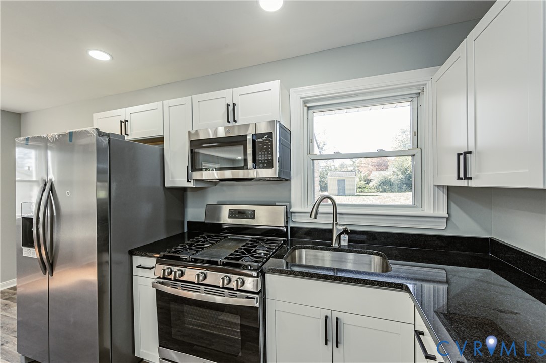 Kitchen featuring white shaker-style cabinetry, dark stone countertops, stainless steel appliances, a gas range, and an undermount sink with a gooseneck faucet