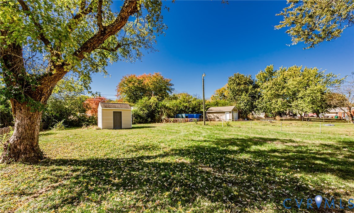 Expansive yard featuring mature trees, a detached storage structure, and a fenced perimeter