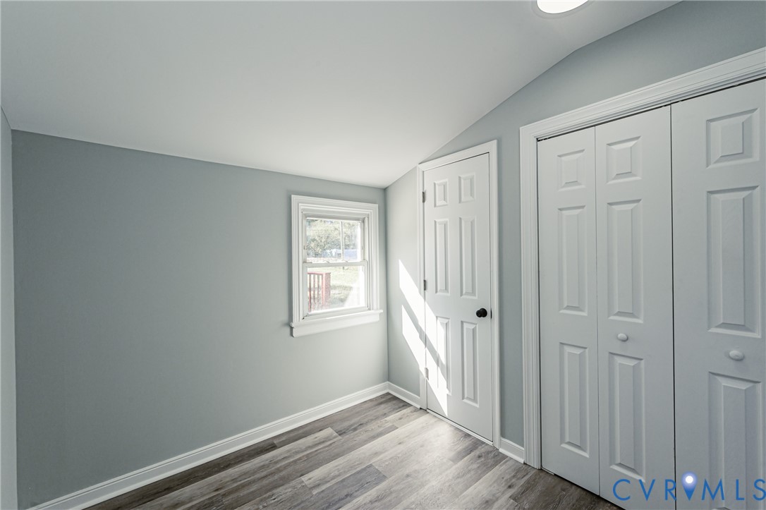 Room featuring wood-finish flooring, a single window, a six-panel interior door, and a built-in closet with bifold doors