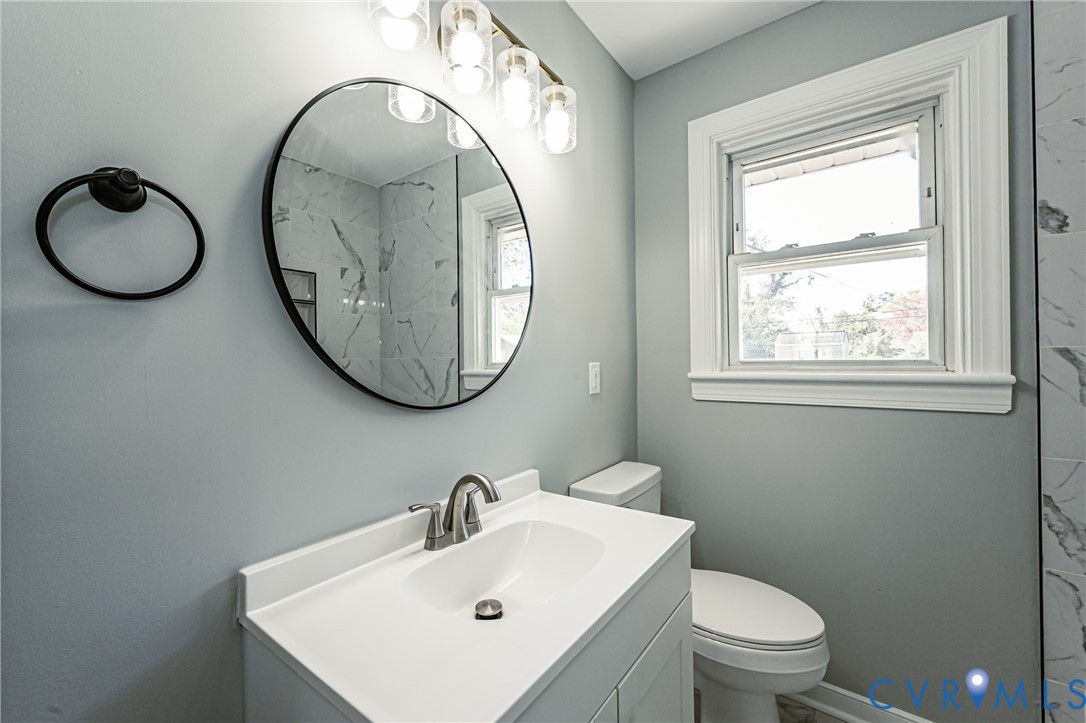 White vanity cabinet with an integrated basin, sleek metallic faucet, circular wall-mounted mirror, and multi-bulb light fixture