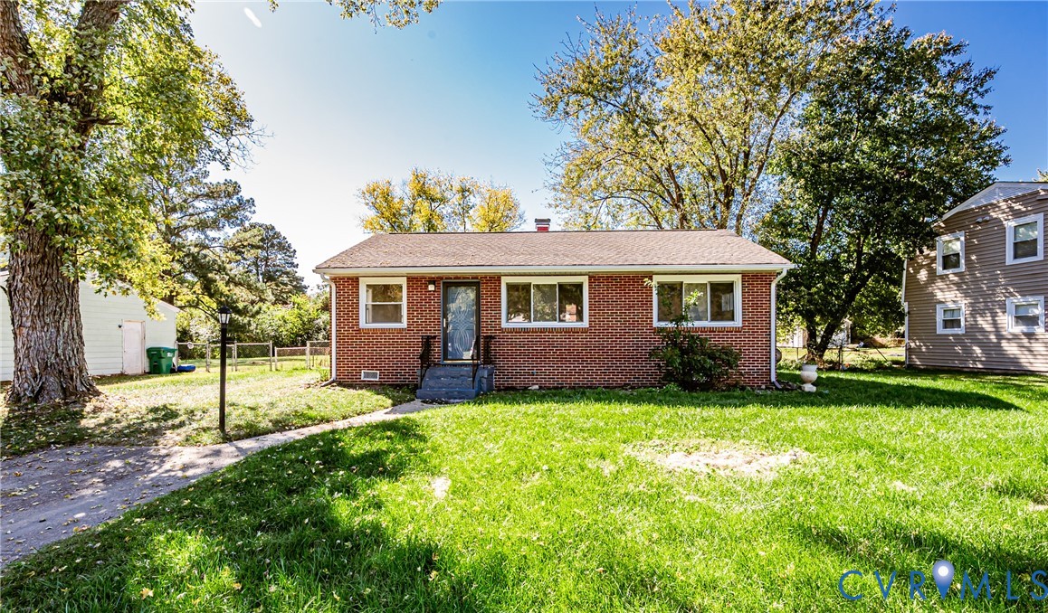 Single-story brick exterior featuring a shingled roof, concrete front steps, and mature trees on a level lot