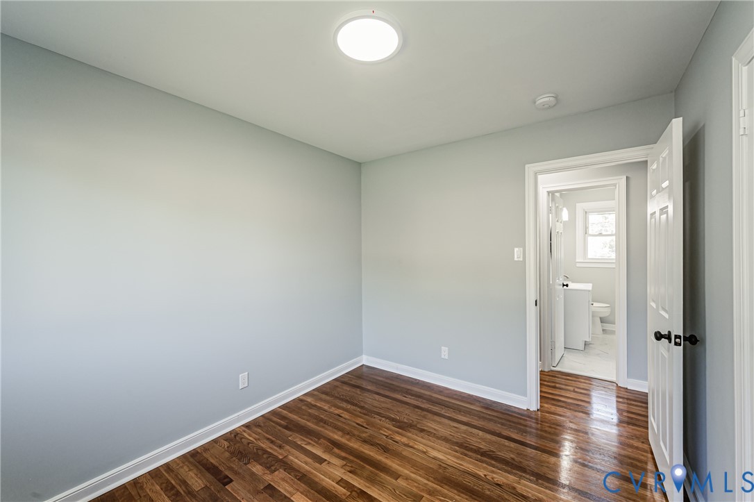 Room featuring light-toned neutral walls, polished wood-finish flooring, and a flush-mount ceiling light fixture