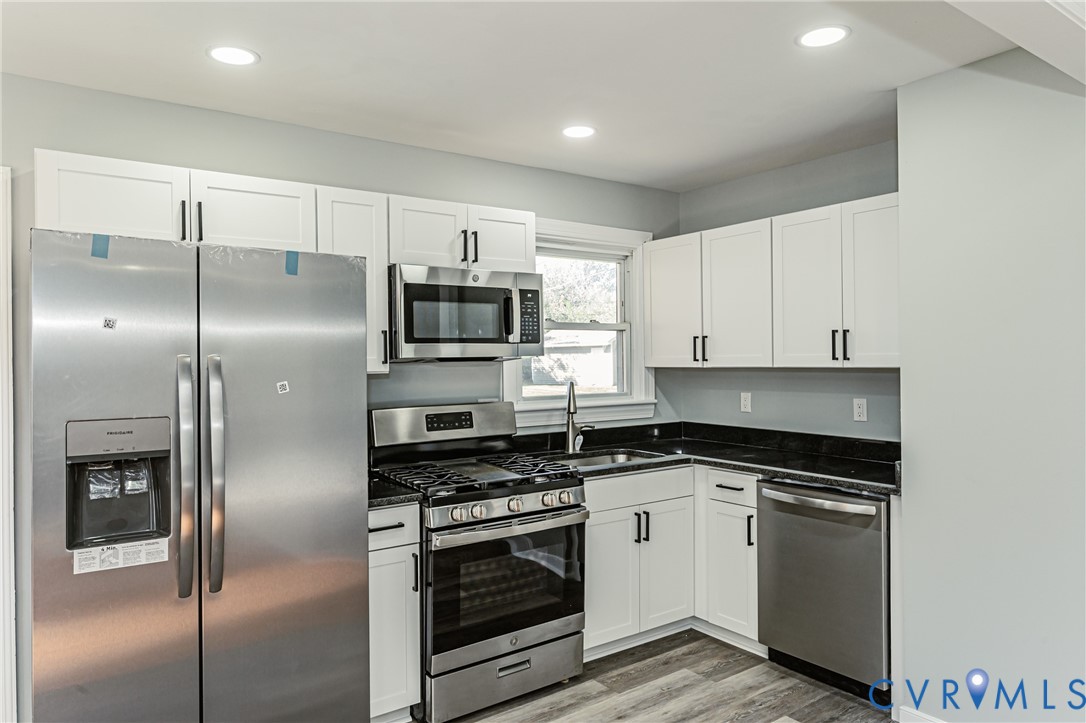 Kitchen featuring white shaker-style cabinetry, stainless steel appliances, dark stone countertops, recessed lighting, and wood-finish flooring