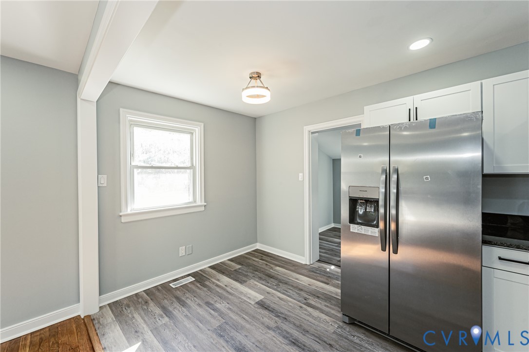 Stainless steel side-by-side refrigerator, white shaker-style cabinetry, wood-finish flooring, recessed lighting, and a flush-mount ceiling fixture