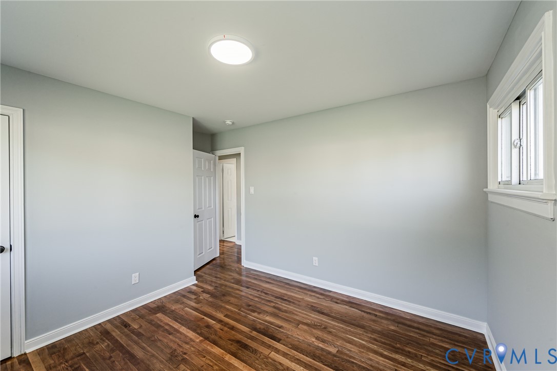 Interior room featuring wood-finish flooring, light gray walls, a sliding window with white casing, and a flush-mount light fixture