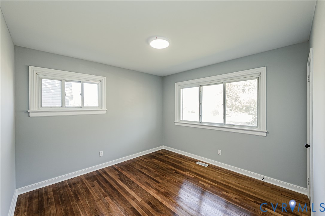 Room featuring wood-finish flooring, dual windows with white trim, and a flush-mount ceiling light fixture