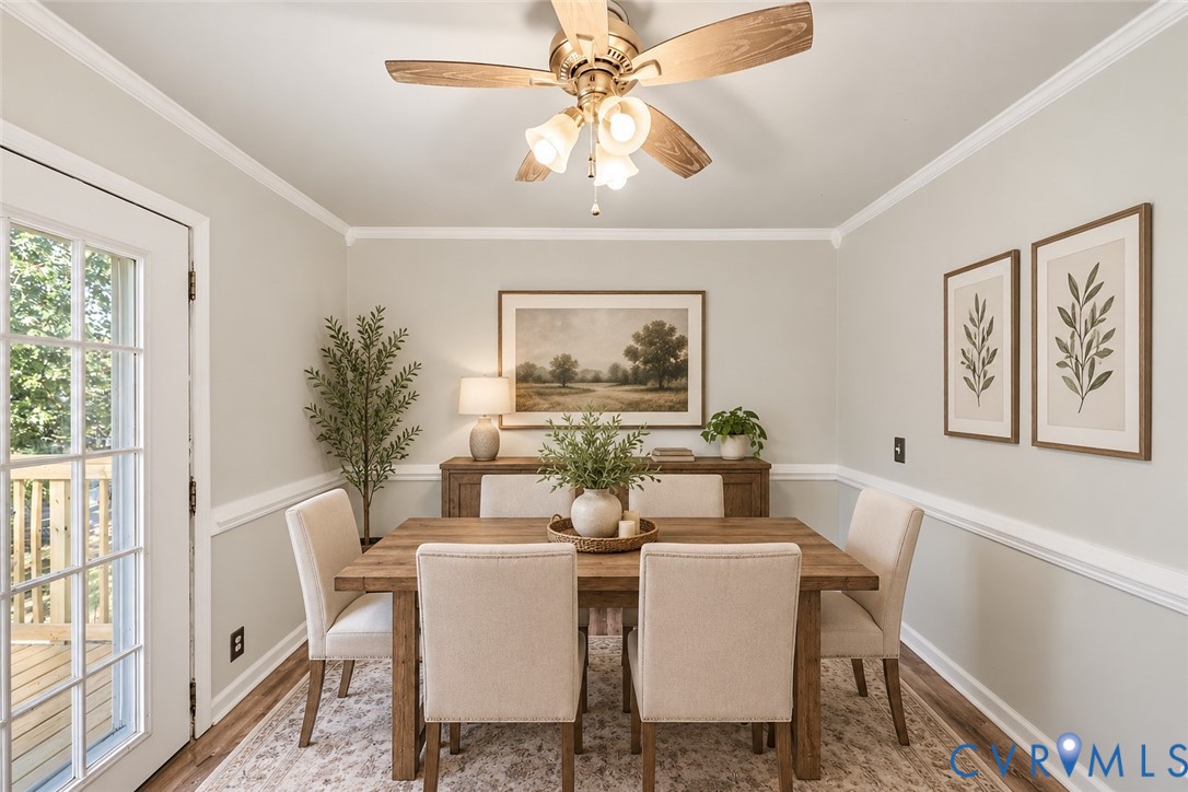 Dining area featuring chair rail molding, crown molding, wood-finish flooring, a multi-light ceiling fan, and a multi-pane glass door, ai staged