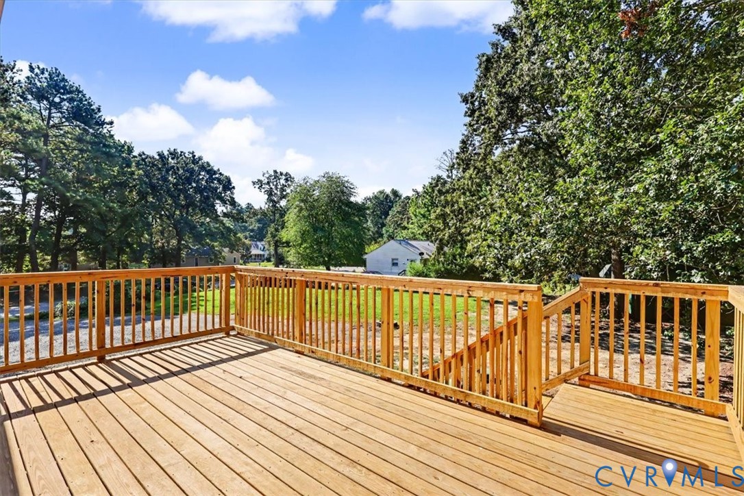Elevated wood deck featuring vertical wood balusters and stairs leading to the grounds, complemented by mature trees