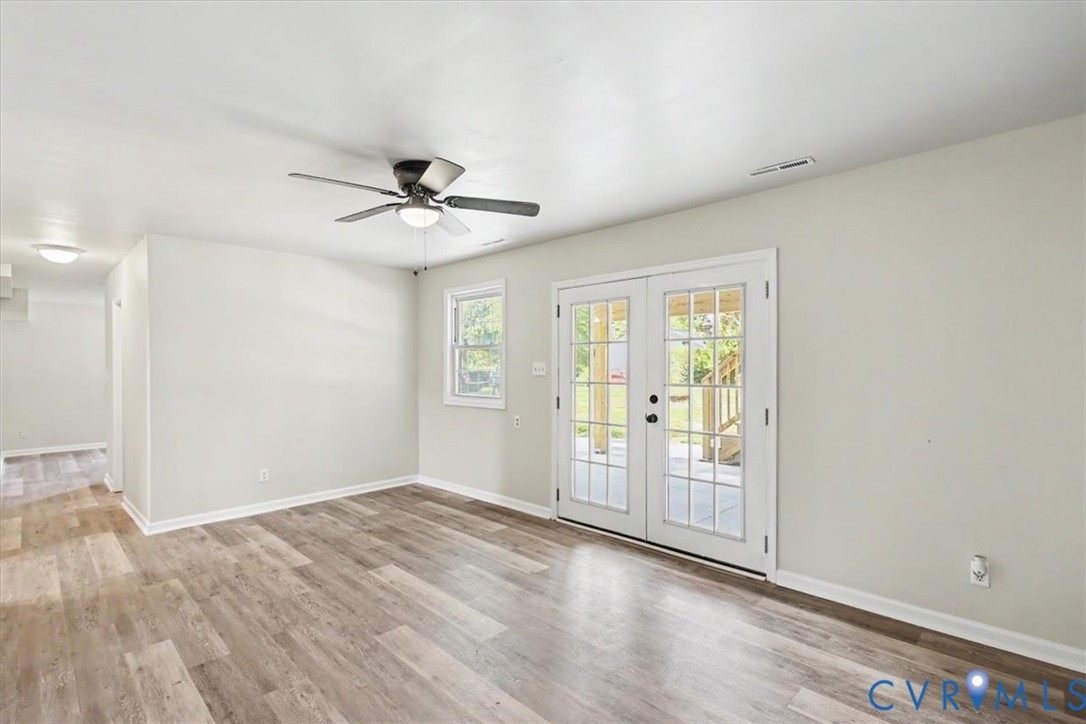 Room featuring wood-finish flooring, glass-paned double doors, a ceiling fan with integrated lighting, and neutral wall tones