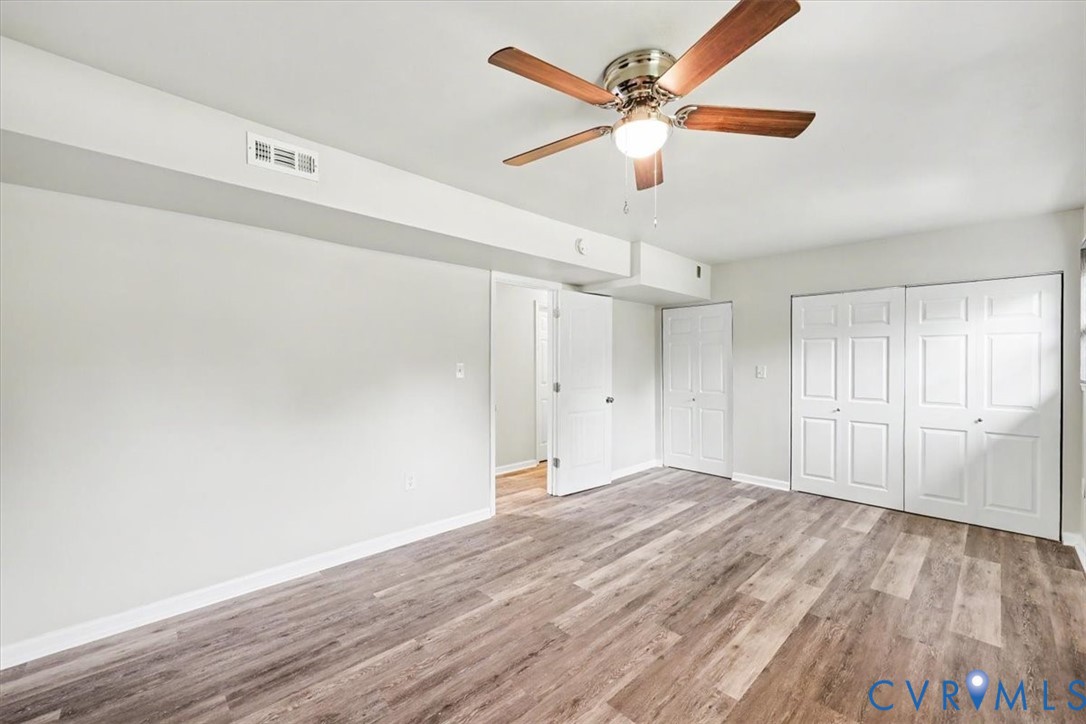 Room featuring wood-finish flooring, a ceiling fan with integrated lighting, and dual sets of white panel doors