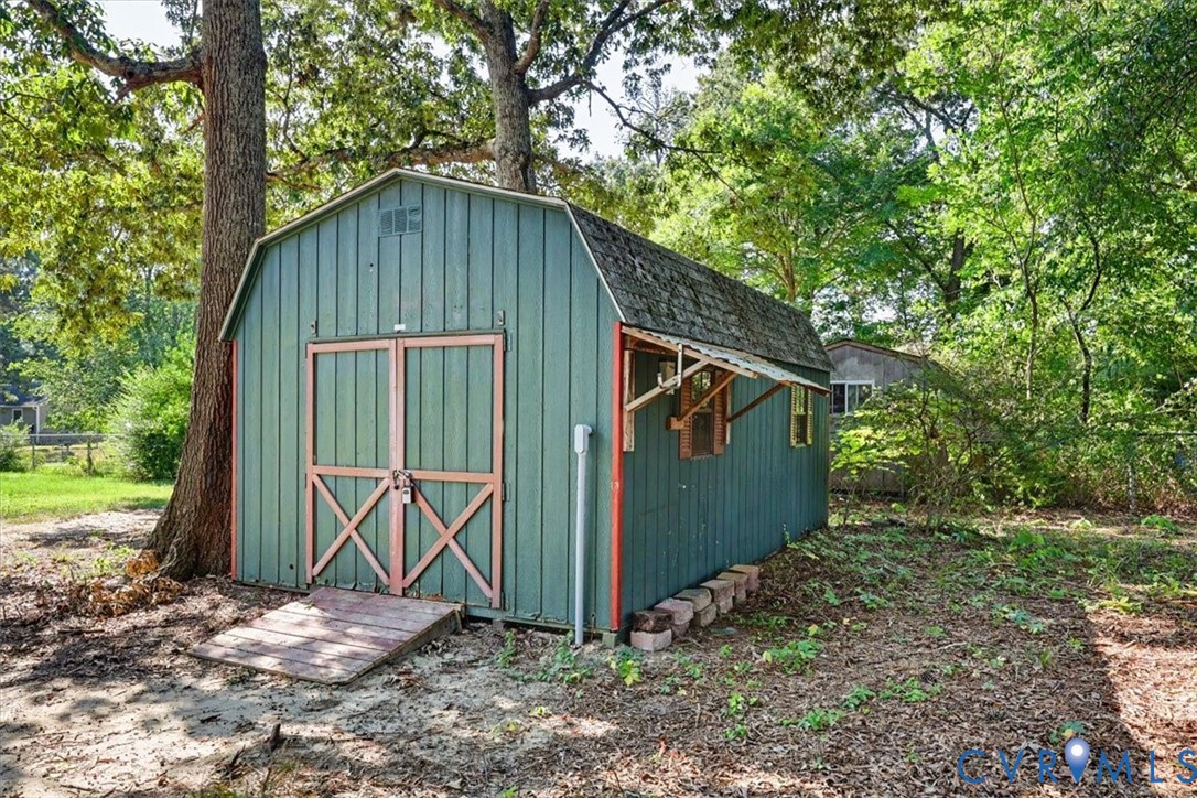 Exterior storage structure with a gambrel roof, metal siding, double-door entry, and a wood-slat ramp