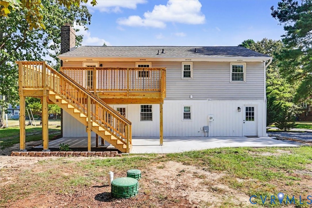 Two-story exterior featuring light-toned horizontal siding, a raised wood deck with stair access, a ground-level concrete patio, and a brick chimney