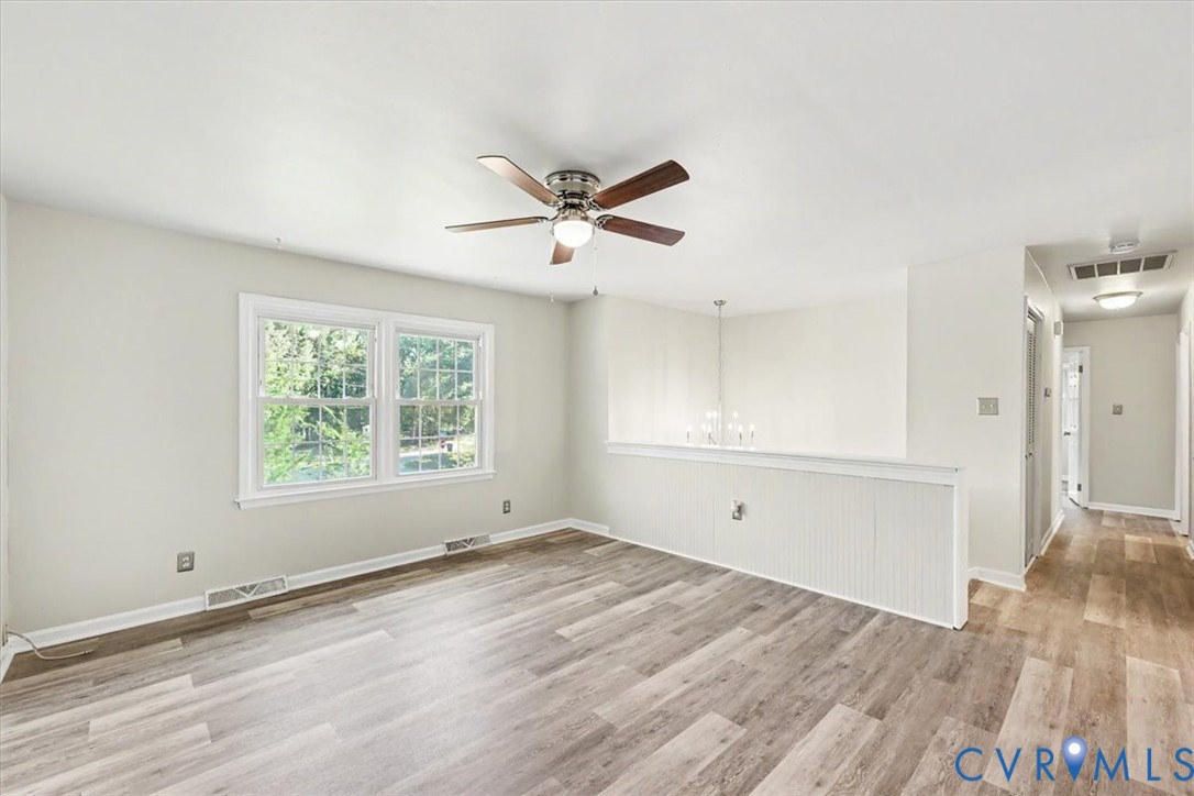 Neutral interior featuring wood-finish flooring, a multi-blade ceiling fan with integrated lighting, beadboard wainscoting, and large double-pane windows