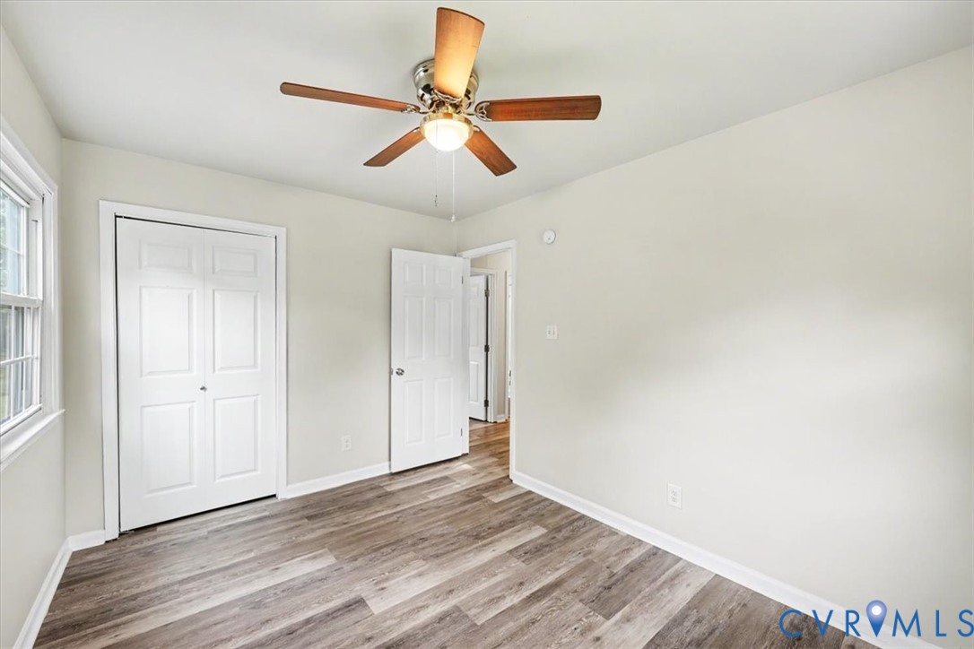 Room featuring wood-finish flooring, a central ceiling fan with integrated lighting, and white six-panel closet doors