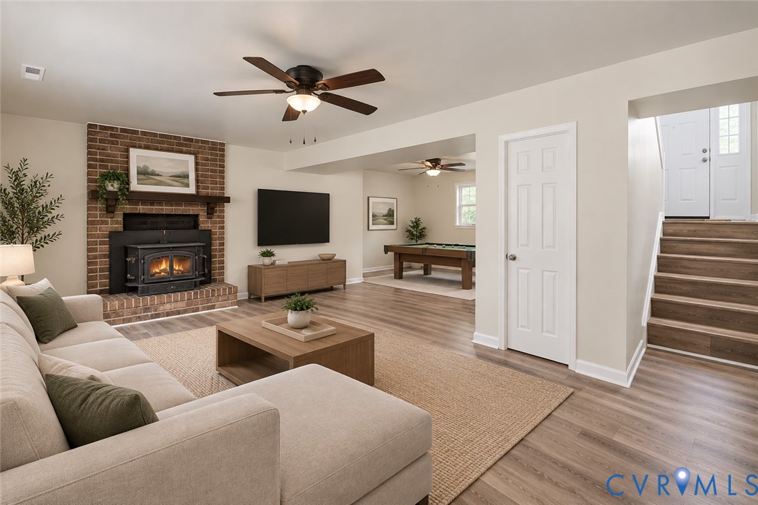 Living area featuring a full-height brick fireplace with a wood-mantel insert, wood-finish flooring, and ceiling fans, ai staged