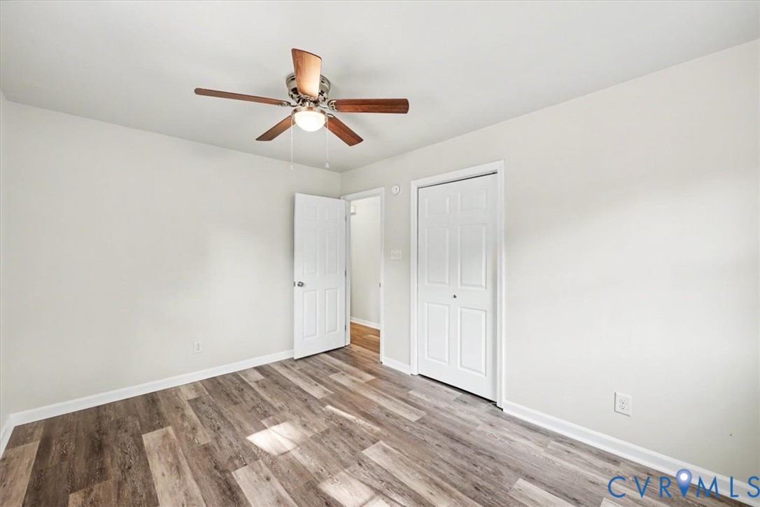 Neutral walls paired with wood-finish flooring, featuring a ceiling-mounted light fixture with fan, six-panel interior door, and double-door closet