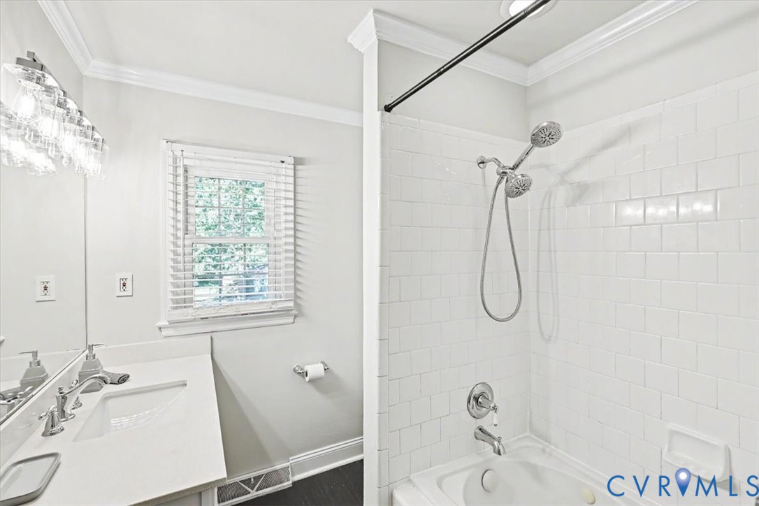 Bathroom featuring a white vanity with a rectangular sink, multi-light fixture, tiled tub-shower surround, and a handheld shower head