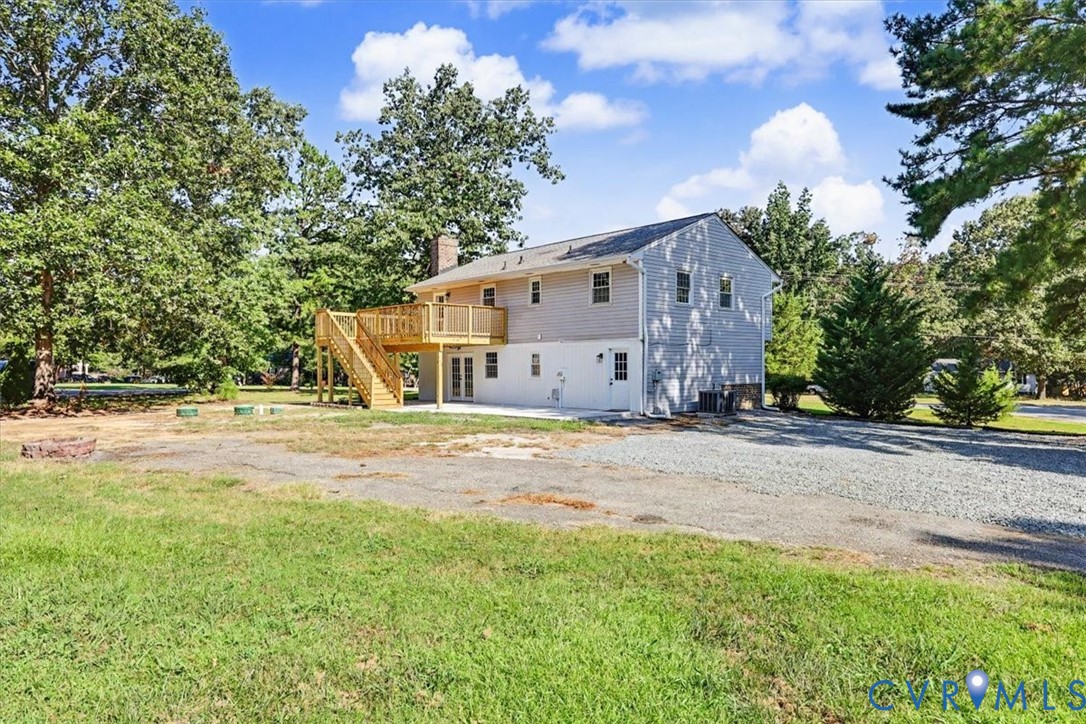 Two-story exterior featuring light-toned horizontal siding, a raised wood deck with stair access, a stone chimney, and a gravel driveway