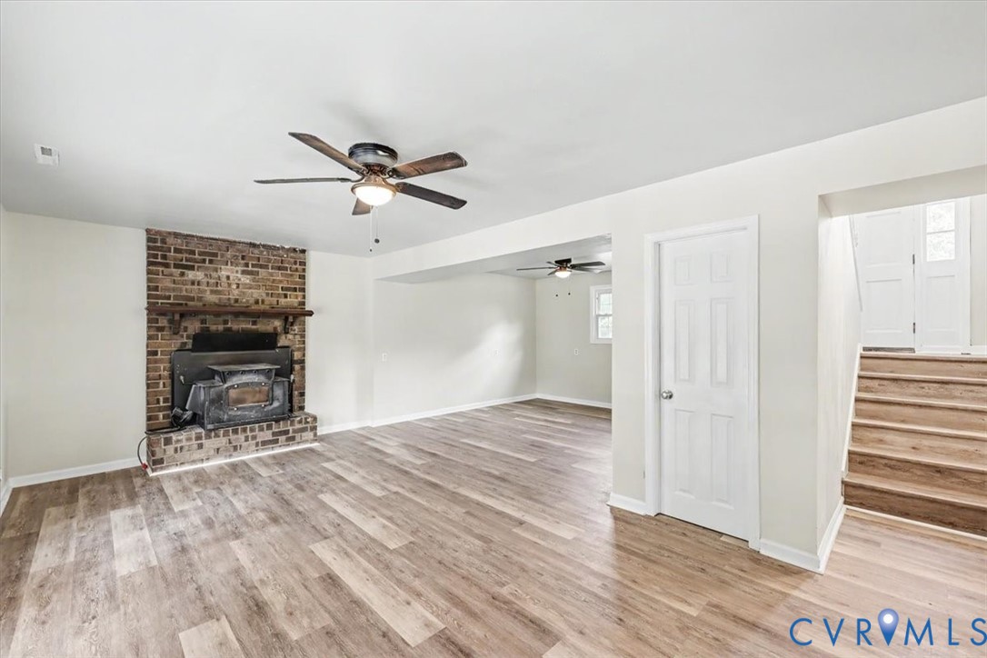 Living area featuring wood-finish flooring, a floor-to-ceiling brick fireplace with a wood mantel, a ceiling fan, and a staircase with wood treads