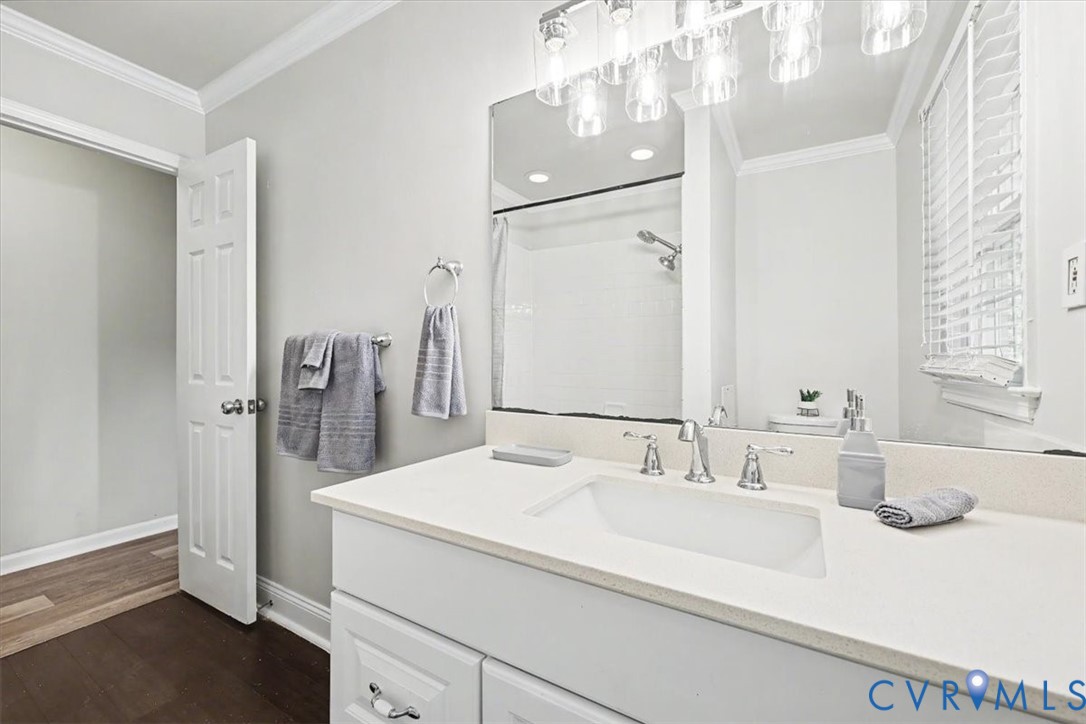 Bathroom featuring a white vanity with a composite countertop, undermount sink, multi-light fixture, large wall mirror, and shower with a tub enclosure