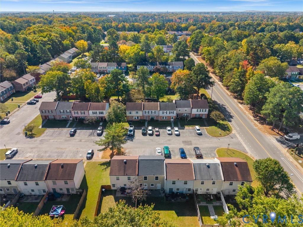 Aerial perspective of townhome community featuring multi-story brick and siding facades, asphalt parking areas, and manicured green space with mature trees