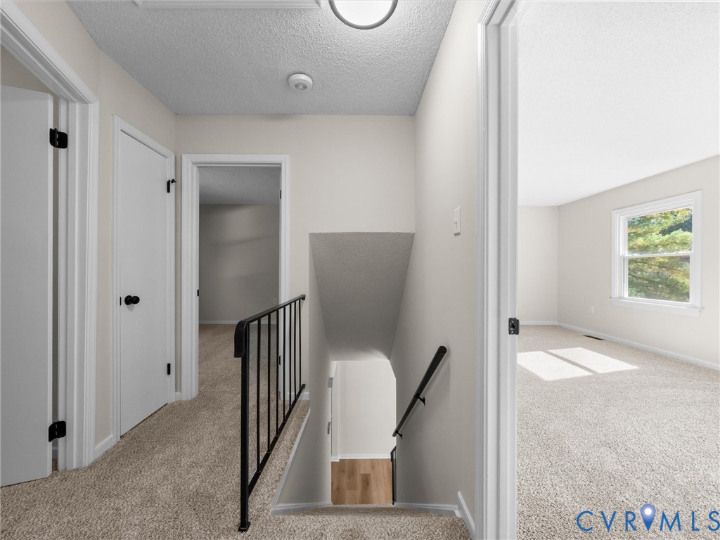 Neutral-toned interior featuring wall-to-wall carpeting, metal stair railing with a coordinating handrail, and multiple interior passage doors