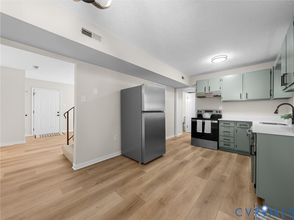 Kitchen featuring wood-finish flooring, stainless steel appliances, light-toned cabinetry, and solid-surface countertops