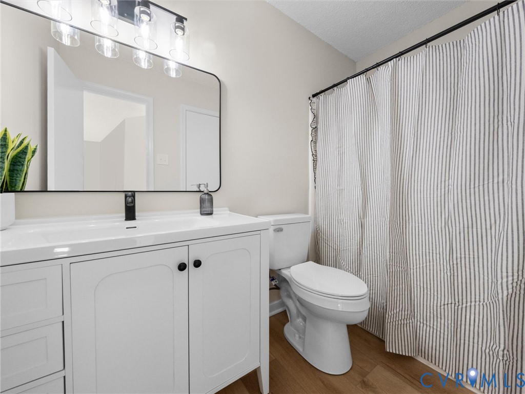 White vanity with integrated basin, matte black faucet, rounded rectangular mirror with a black frame, multi-bulb vanity light fixture, and wood-finish flooring