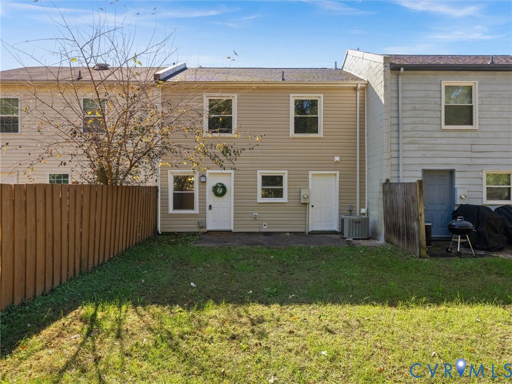 Rear exterior featuring tan siding, a private fenced yard, a concrete patio, and exterior light fixtures