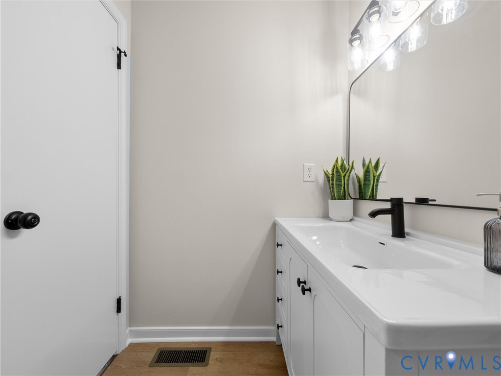 White vanity featuring an integrated sink, matte black faucet, and matte black hardware, paired with a rectangular wall-mounted mirror and multi-bulb vanity lighting