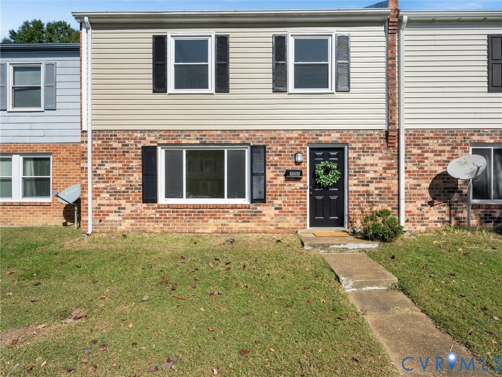 Two-story exterior featuring a combination of brick and vinyl siding, horizontal window shutters, and a concrete walkway