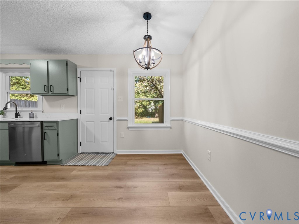 Kitchen featuring sage green cabinetry, stainless steel dishwasher, wood-finish flooring, chair rail molding, and a spherical metal chandelier
