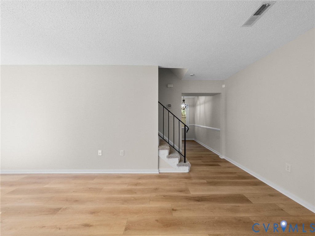Neutral-toned interior featuring wood-finish flooring, staircase with metal railing, and textured ceiling