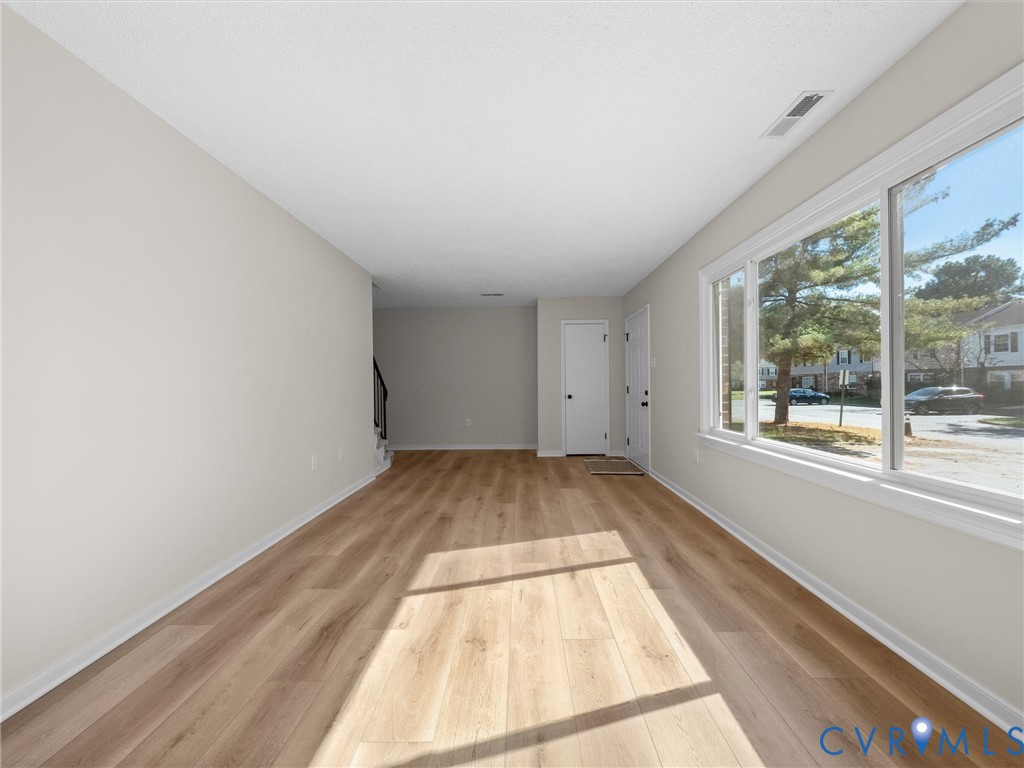 Neutral-toned interior space featuring wood-finish flooring, white walls, and a large horizontal window