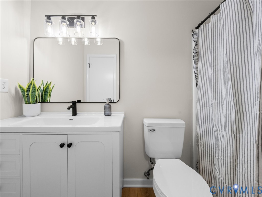 White vanity featuring a rectangular integrated sink, matte black faucet, rounded rectangular mirror, and multi-bulb industrial light fixture