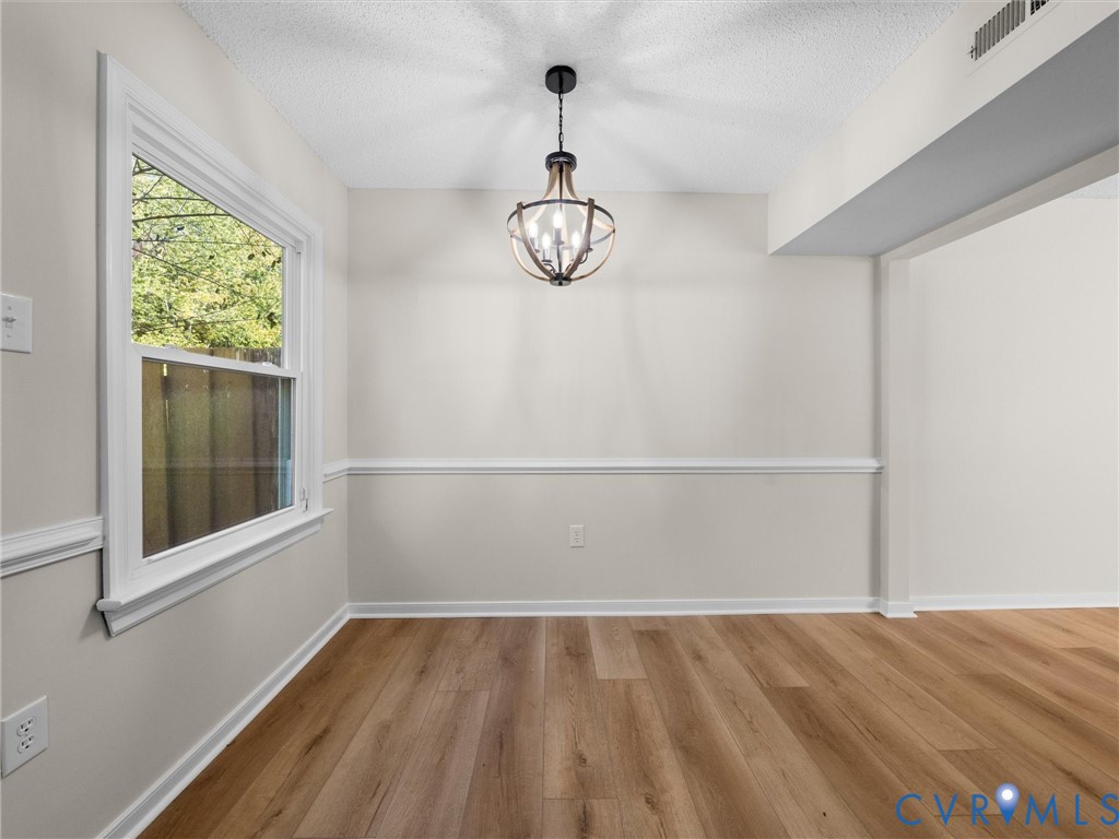 Room featuring wood-finish flooring, wainscoting, a single-hung window, and a multi-arm orb-style light fixture