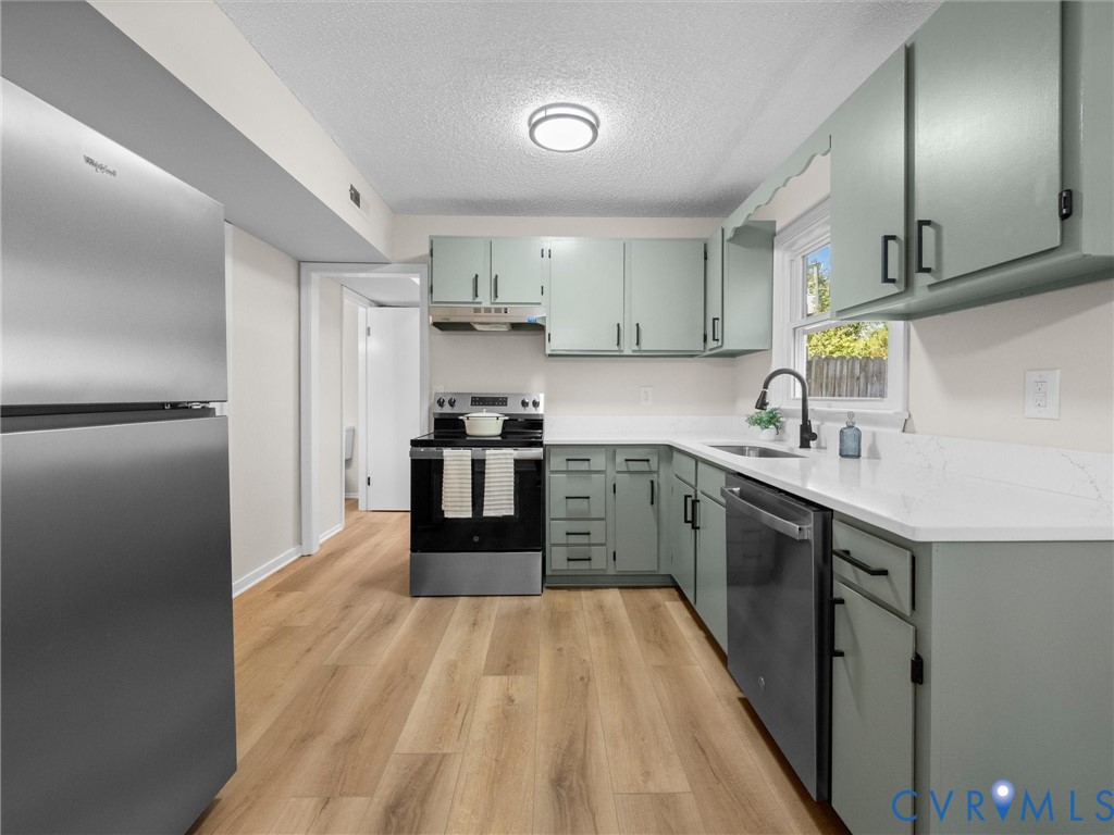 Kitchen featuring light green cabinetry, white stone-finish countertops, stainless steel appliances, and wood-finish flooring