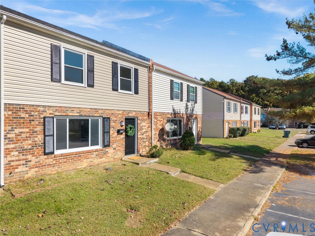 Multi-level exterior featuring a brick and vinyl siding faade, dark window shutters, and a concrete walkway