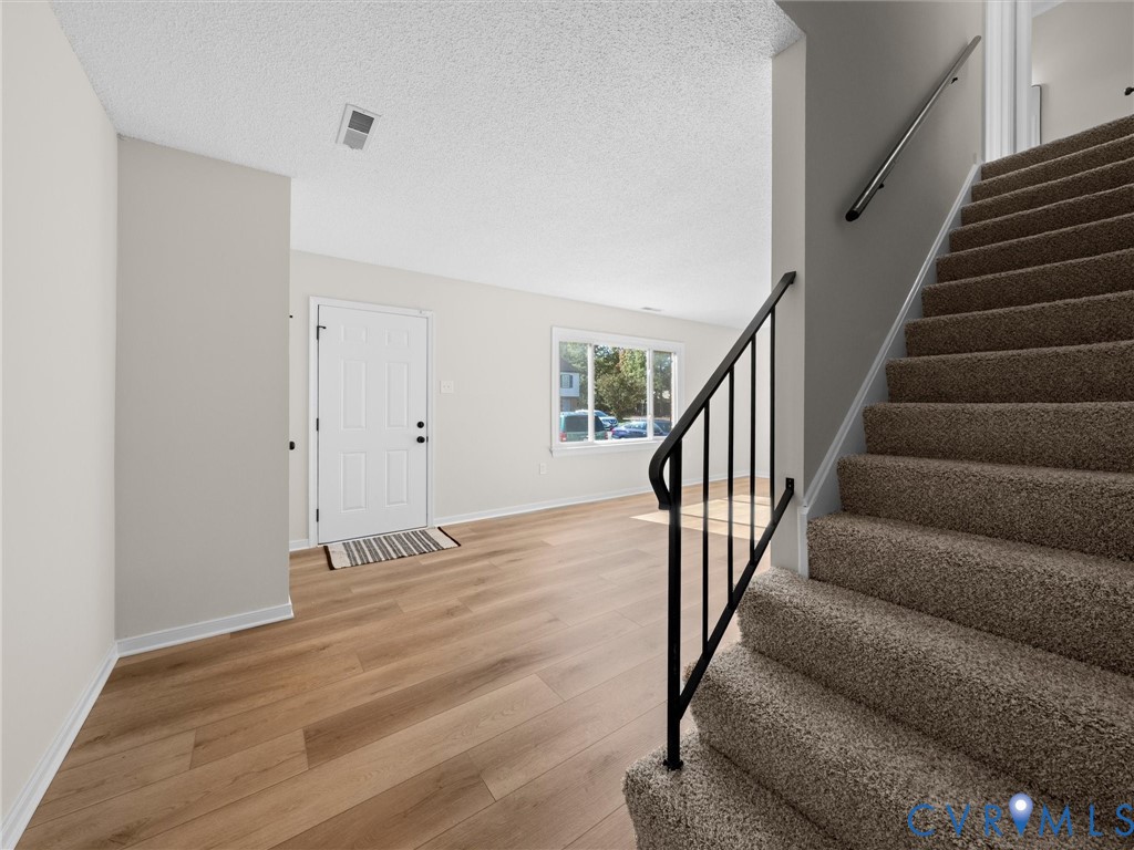 Entryway featuring wood-finish flooring, a neutral color palette, and a staircase with carpeted treads and a metal handrail