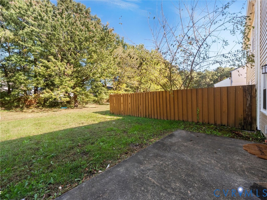 Rear yard featuring a concrete patio, wood-finish privacy fencing, and mature trees
