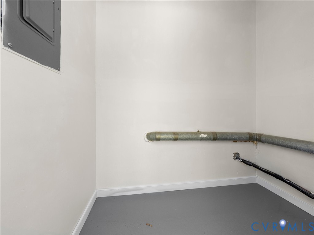 Utility area featuring painted walls, exposed piping, and a central electrical panel