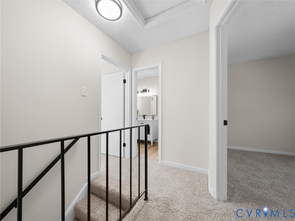 Hallway featuring neutral wall tones, wall-to-wall carpeting, metal stair railing, and multiple interior doorways