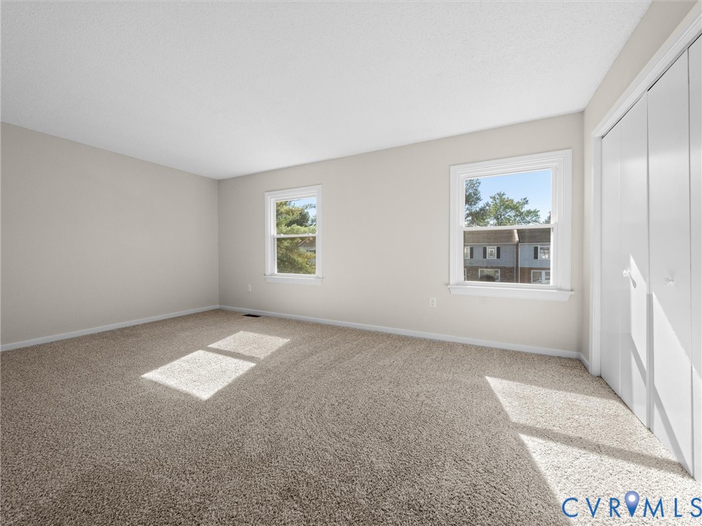 Room featuring wall-to-wall carpeting, dual windows, neutral paint, and built-in closet storage with double-panel doors